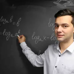 Mężczyzna pisze kredą wzory logarytmiczne na tablicy.