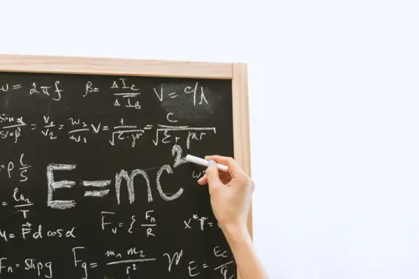 Tablica z równaniami fizycznymi, gdzie widać słynne E=mc². Ręka pisze kredą, a obok widnieje znak mniejsze lub równe.